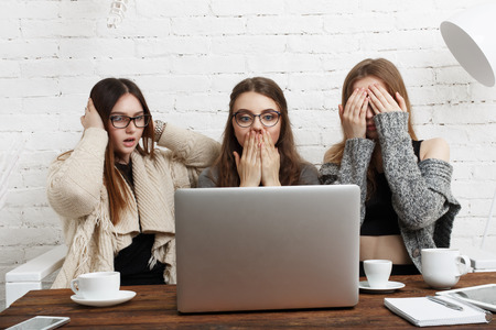 Three young women with computer showing blind, deaf and dumb: three wise monkey scene - hear no evil, see no evil, speak no evil. Girls look at monitor show indifference, negation, silence.の写真素材
