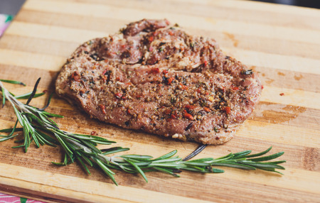 Fresh pork steak ready for BBQ cooking. Raw meat on a cutting board with rosemary leaf. Raw pork meat on wood, closeup. Marinated in spices raw steak for barbecue.の写真素材