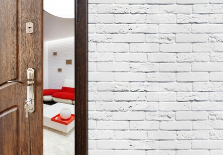 Half opened door to a living room. Door handle, door lock. Lounge door half open. Opening door. Welcome, privacy concept. Entrance to the room. Door at white brick wall, modern interior design.の写真素材