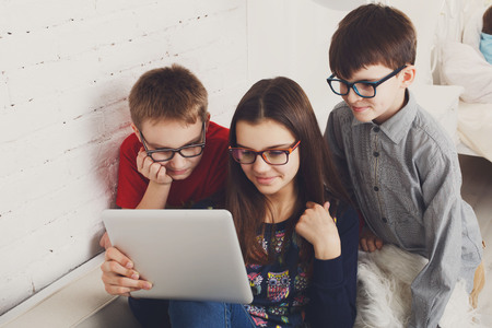 Group of kids in eye glasses look into tablet. Children computer games, social networks and media...