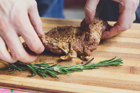 Chef hands hold fresh pork steak ready for BBQ cooking. Raw meat on a cutting board with rosemary leaf.の写真素材