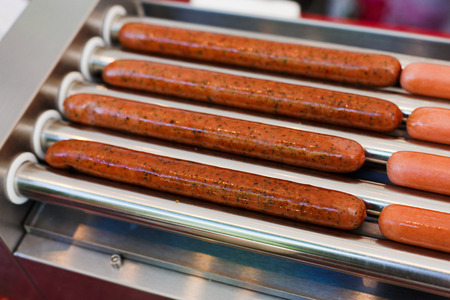 Hot dog machine closeup. Sausages grill at hot dog maker. Professional equipment for hot dog preparation. Various sausages, wurst at grill.の写真素材