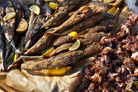 Plenty of seafood, fish, octopus grilled at barbecue. Mackerel and other seafood bbq outdoors at picnic, party. Street food, seafood takeaway at big tray. Grill at bamboo sticks.の写真素材