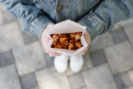 Child with popcorn in hands. Sweet sugar caramelized popcorn pack in little girl's hands, POV composition. Top view of child with popcorn outdoors, sweet snack, street food, fast food.の写真素材