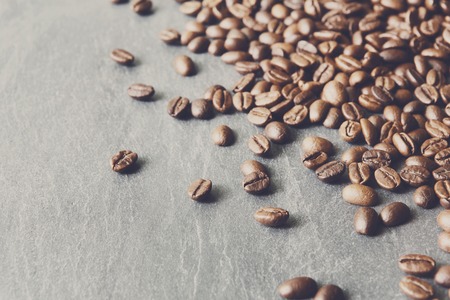 Closeup of coffee beans on grey stone surface. Heap of roasted coffee bean on stone texture with copy space. Coffee shop or cafe background. Natural stone and seeds. Soft color toningの写真素材