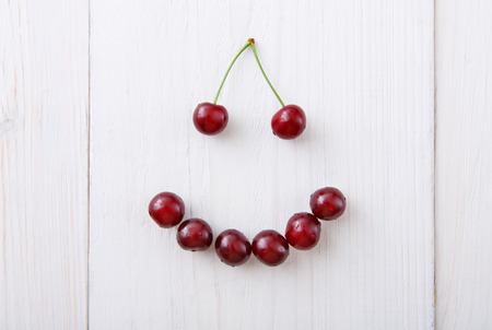 Smiley face from sweet fresh cherries. Smile sign from healthy food. Fruits closeup on white rustic wood pattern.の写真素材