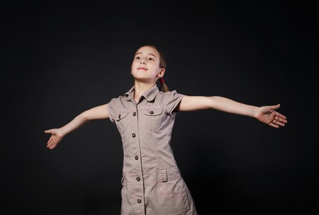 Small cute girl openes hands in fly gesture at black background. Portrait of little female child dreamingの写真素材