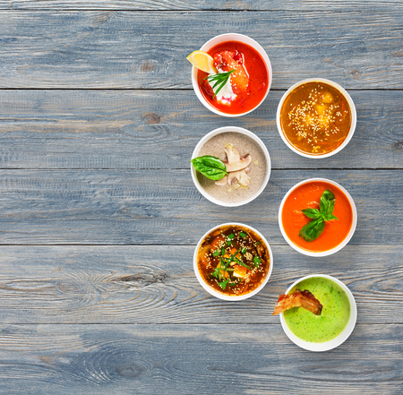 Variety of restaurant hot dishes, healthy food. Japanese miso, asian fish soup, russian borscht, english pea soup with bacon, mushroom soup, spanish gazpacho at blue wood, top view with copy spaceの写真素材