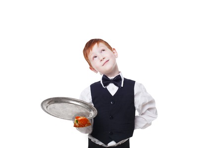 Clumsy little waiter drops tray with small pizza piece while dreaming. Food falling down. Redhead child boy in suit shows inattentive waiter failure at white backgroundの写真素材