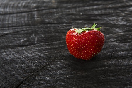 Red fresh strawberry on black rustic wood background. One natural ripe organic berry with peduncle on wooden surface, view with copy spaceの写真素材