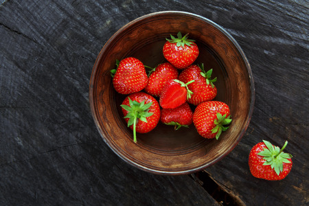 Red fresh strawberries on black rustic wood background. Bowl with natural ripe organic berries with peduncles on wooden circle cut out, top view with copy spaceの写真素材