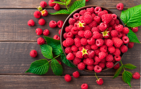 Red fresh raspberries on brown rustic wood background. Bowl with natural ripe organic berries with...