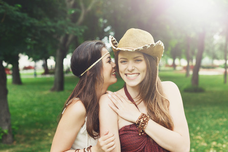 Two happy young girls gossiping and laughing. Women friendship, walk in the park outdoors. Caucasian boho girl with asian friendの写真素材