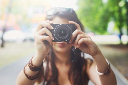 Young asian girl taking photo outdoors with digital camera. Selective focus at lens, unrecognizable person. Young female tourist having fun in summer park. Lifestyle portrait, soft tonedの写真素材