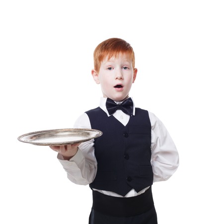 Little waiter stands with tray serving big double hamburger. Smiling redhead child boy in suit plays restaurant servant, gives burger at blue backgroundの写真素材