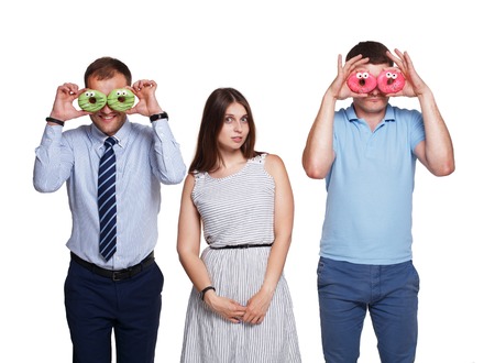Studio shot of young people, men and woman having fun with donuts. Beautiful friends make donut glasses looking at camera and smiling. Isolated at white background.の写真素材