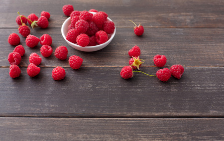 Red fresh raspberries on brown rustic wood background. Bowl with natural ripe organic berries with...
