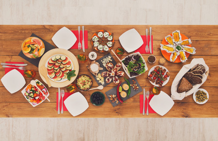 Healthy meals at festive table served for party. Authentic celebration with organic food on wooden table top view. Ratatoille, cheese, corn and chicken barbecue, sandwiches with mojito and lemonadeの写真素材