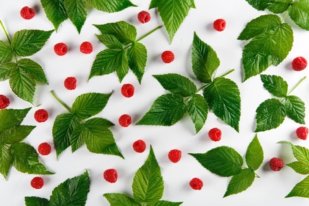 Red fresh raspberries on white background. Scattered natural ripe organic berries with green leaves, top view flat layの写真素材