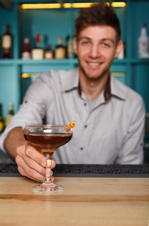 Young handsome Barman offers alcohol cocktail in night club. Professional male bartender at work in...