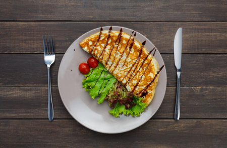 Restaurant food top view on wood. Omelette with vegetables and lettuce on blue plate. Appetizing dish served with sauce, dinner meal. Decorated healthy meal for gourmetの写真素材