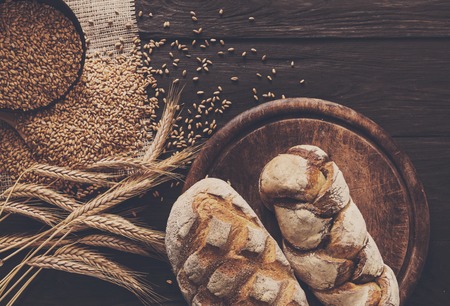 Bread background. Brown and white whole grain loaves composition on rustic wood with wheat ears scattered around. Baking and home bread making concept.の写真素材