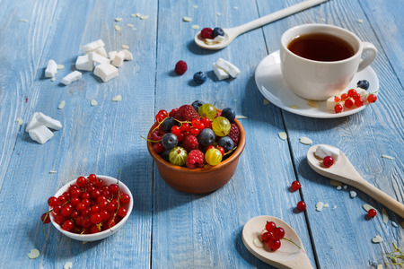 Sweet berries dessert - red currant, gooseberry, raspberry and bluberries. Healthy and natural food, diet nutrition. Beautiful dish served at blue rustic wooden table on white porcelain plateの写真素材