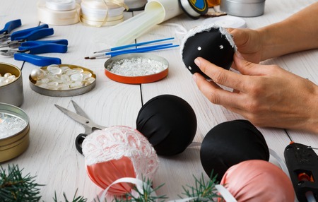 Creative diy hobby. Making handmade craft unusual black stylish christmas balls. Woman's leisure, tools for creating holiday decorations. Female hands closeup working on white wooden tableの写真素材