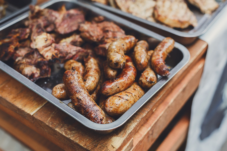 Sausage party. Plenty of roasted at barbecue wurst and grilled kielbasa in metal container for sale at country fair. Picnic bbq food outdoors.の写真素材