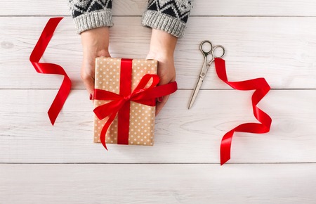 DIY hobby. Woman's hands give wrapped christmas or other holiday handmade present in paper with red...
