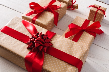 Lots of Gift boxes on white wood background. Presents in craft paper decorated with red ribbon bows....