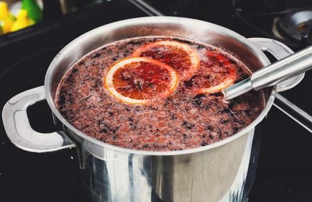 Making mulled wine for sale at country fair. Glintwine with citrus and cloves in big metal stock pot, mixed with soup ladle.の写真素材