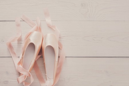 Pastel pink ballet shoes background. New pointe shoes with satin ribbon lay on white rustic shubby chic wood, top view with copy space, soft toningの写真素材