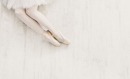 Ballet background. Closeup of young ballerina legs in pointe shoes on white wooden floor, top view from above with copy space. Ballet practice. Beautiful slim graceful feet of dancer.の写真素材