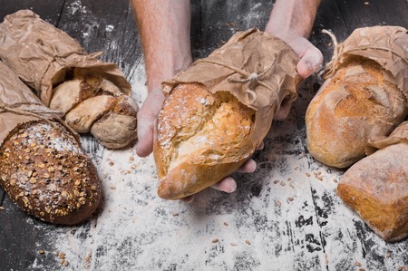 Lots of different bread sorts, wrapped in craft paper. Baking and cooking concept background. Hands...
