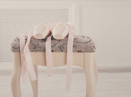 Pastel pink ballet shoes background. New pointe shoes with satin ribbon lay on chairの写真素材