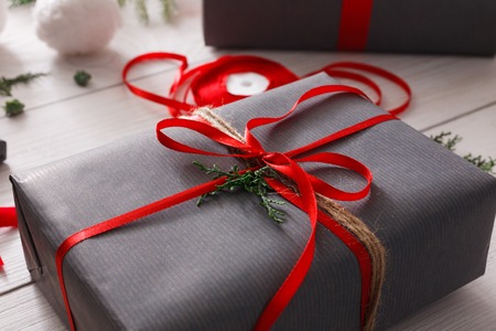 Creative diy hobby. Handmade tools for making modern christmas present, boxes in stylish gray paper with red satin ribbon. Messy white wooden table closeup with fir tree branches, decoration of gift.の写真素材