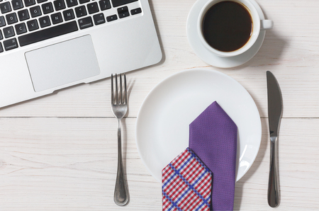 Diet or lack of money concept - no food at business lunch in the office. Top view of working space at white wooden desk, empty plate with tie, americano coffee cup and cutlery near laptopの写真素材