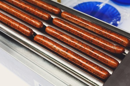 Hot dog machine closeup. Sausages grill at hot-dog maker. Professional equipment for hotdog preparation. Spicy smoked sausages, wurst at grill.の写真素材