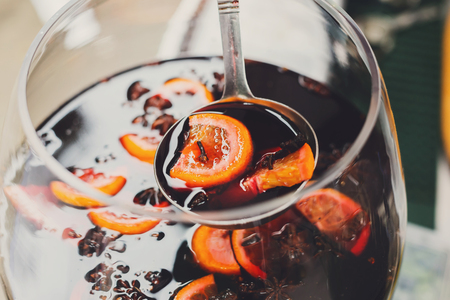 Making hot alcohol, mulled wine for sale at country fair. Glintwine from red wine with citrus and cloves in big glass, mixed with soup ladle. Closeupの写真素材