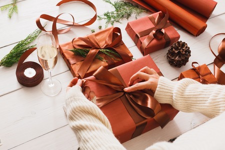 Gift wrapping background. Female hands packaging stylish christmas present boxes in maroon paper decorated with satin ribbon bows. Christmas and winter holidays concept. Still lifeの写真素材