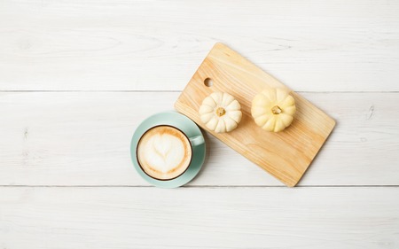 Pumpkin spice latte. Blue coffee cup with foam and small yellow pumpkins at white wood background. Autumn fall hot drinks, cafe and bar concept, top view with copy spaceの写真素材