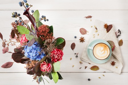 Autumn cappuccino composition. Blue coffee cup top view with foam, cloves, dried flowers bouquet at white wood background with copy space. Fall hot drinks, cafe and bar conceptの写真素材