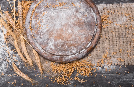Bread baking background. Grain and ears scattered around on rustic wood near round wooden desk sprincled with flour. Agricultural wheat harvest, bread making compositionの写真素材