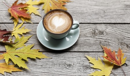 Autumn leaves and cappuccino composition. Blue coffee cup with foam, at weathered rustic wood background with copy space. Fall hot drinks conceptの写真素材