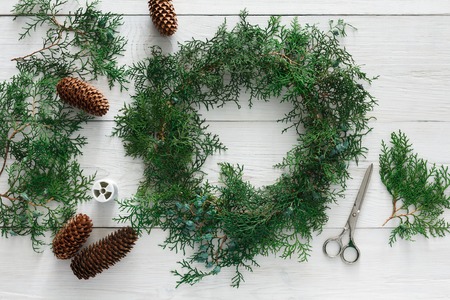Creative diy craft hobby. Making handmade craft christmas ornaments and thuja tree garland. Home leisure, pine cones and tools for holiday decorations. Top view of white wooden tableの写真素材