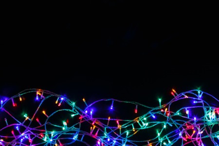 Christmas lights background. Holiday shiny garland border top view on black. Xmas tree decorations, winter holidays illuminationの写真素材