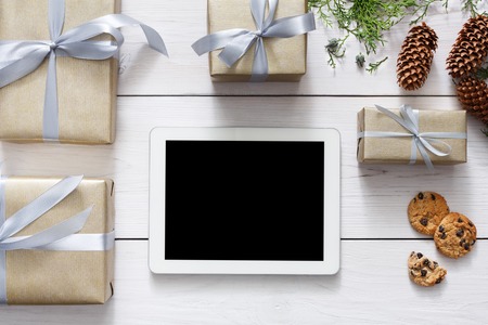 Christmas online shopping background. Tablet screen with copy space top view on white wood, present...