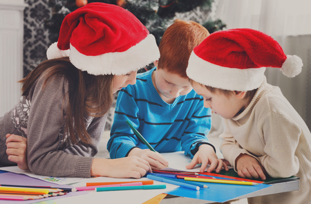 Writing letter to santa. Adorable children in santa hats make wish list of presents for christmas. Waiting for gift. Prepare for winter holidays. Boys and girl, brothers and sister in decorated roomの写真素材