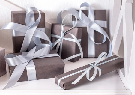 Elegant gift boxes with satin ribbon wrapped in paper. Closeup on white shelves in modern interior....